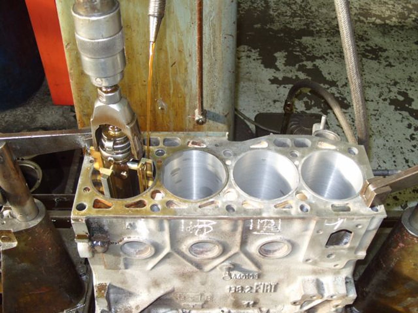 Un bloc moteur à trois cylindres est usiné par une machine d'alésage, avec de l'huile qui coule sur l'outil dans un atelier de mécanique.