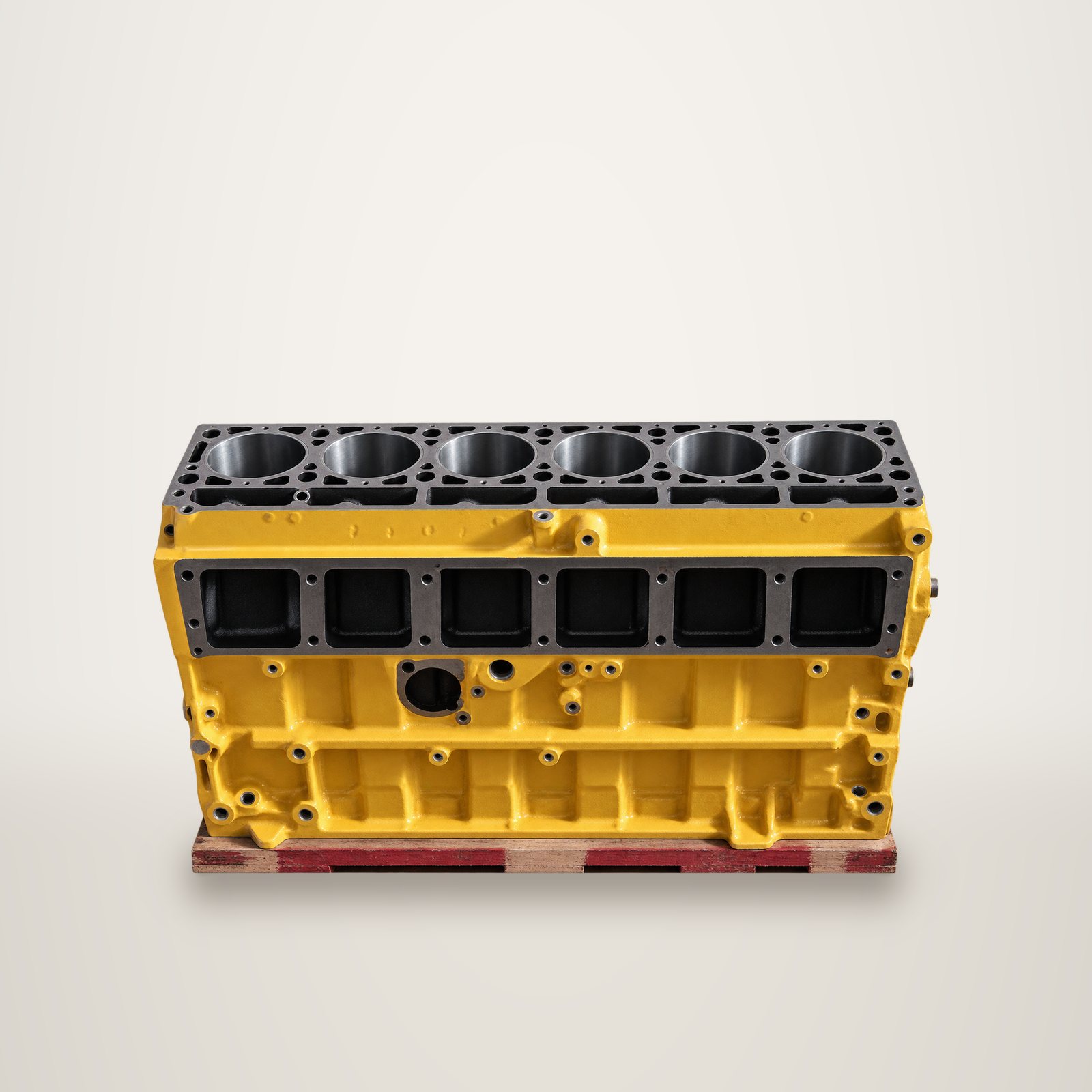 Un bloc moteur jaune à six cylindres, vu de dessus et de côté, posé sur une palette devant un fond uni.