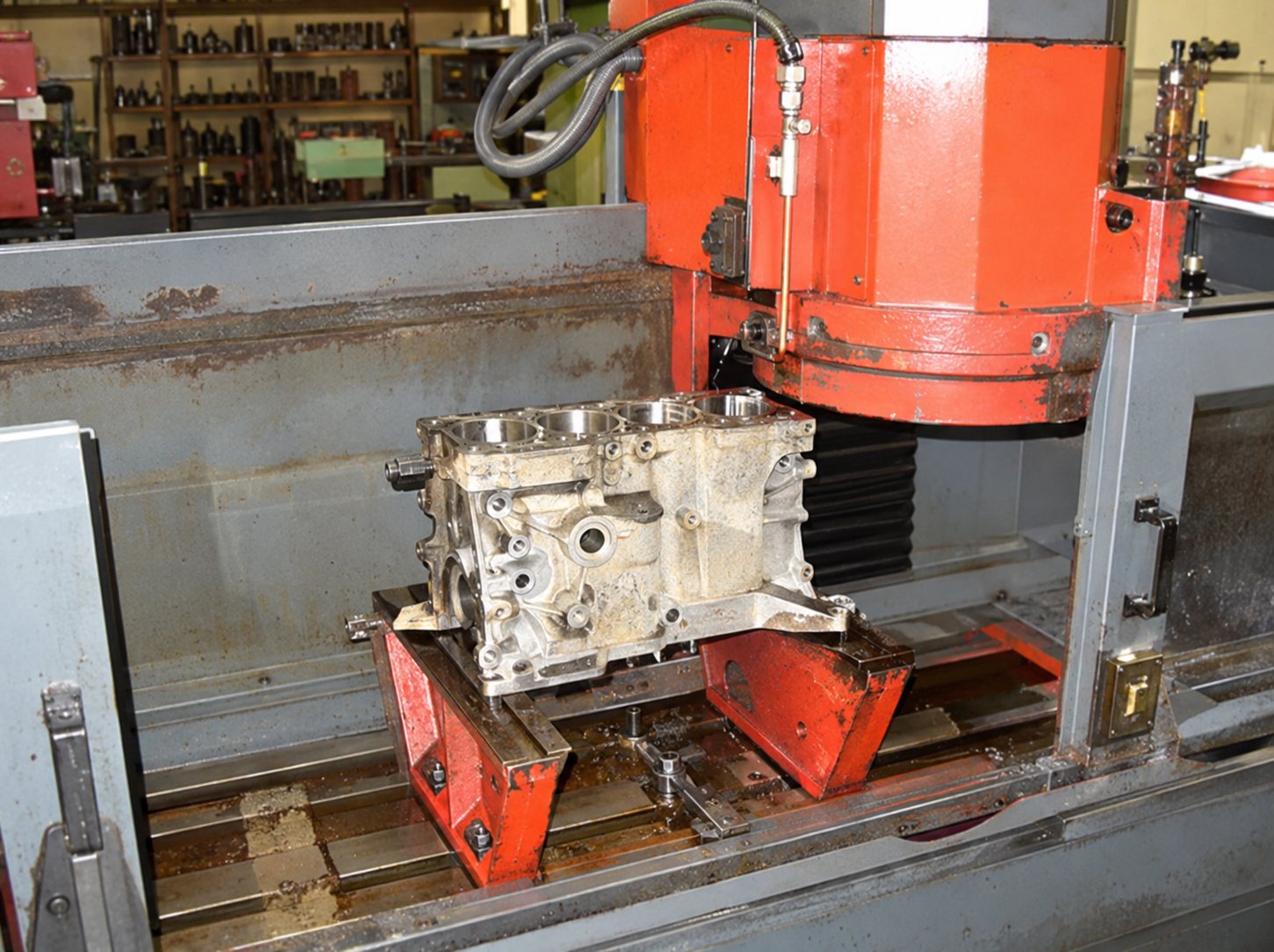 Un bloc moteur en métal est posé sur le plateau d'une grande machine d'usinage rouge dans un atelier de mécanique.