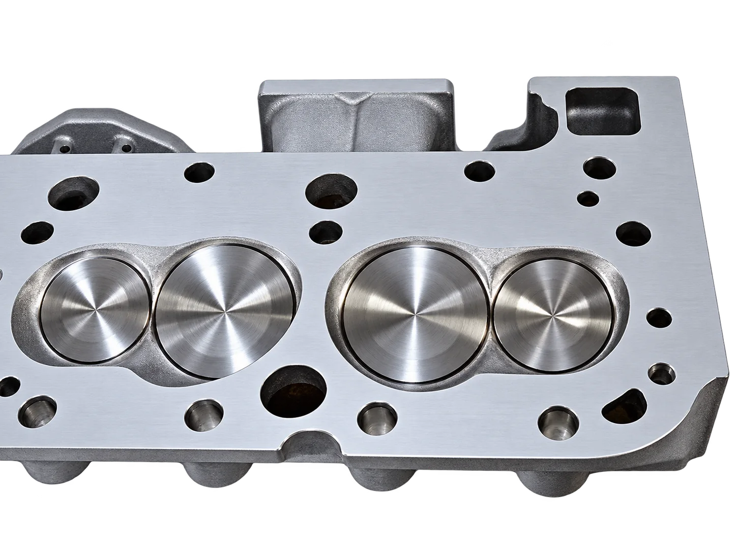 Gros plan sur une culasse de moteur en aluminium usinée, posée sur un fond blanc, montrant les chambres de combustion et les trous de boulons.