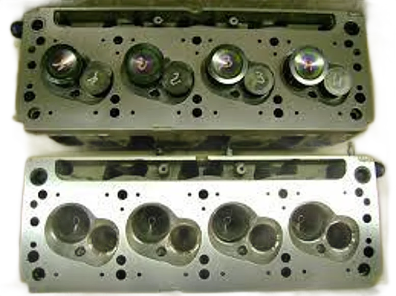 Deux culasses de moteur en aluminium posées côte à côte sur une surface plane, l'une montrant les soupapes numérotées et l'autre les chambres de combustion.