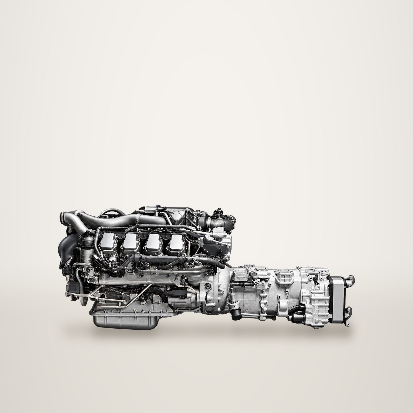 Un moteur diesel V8 de poids lourd associé à sa boîte de vitesses, présenté en suspension sur un fond gris uni.