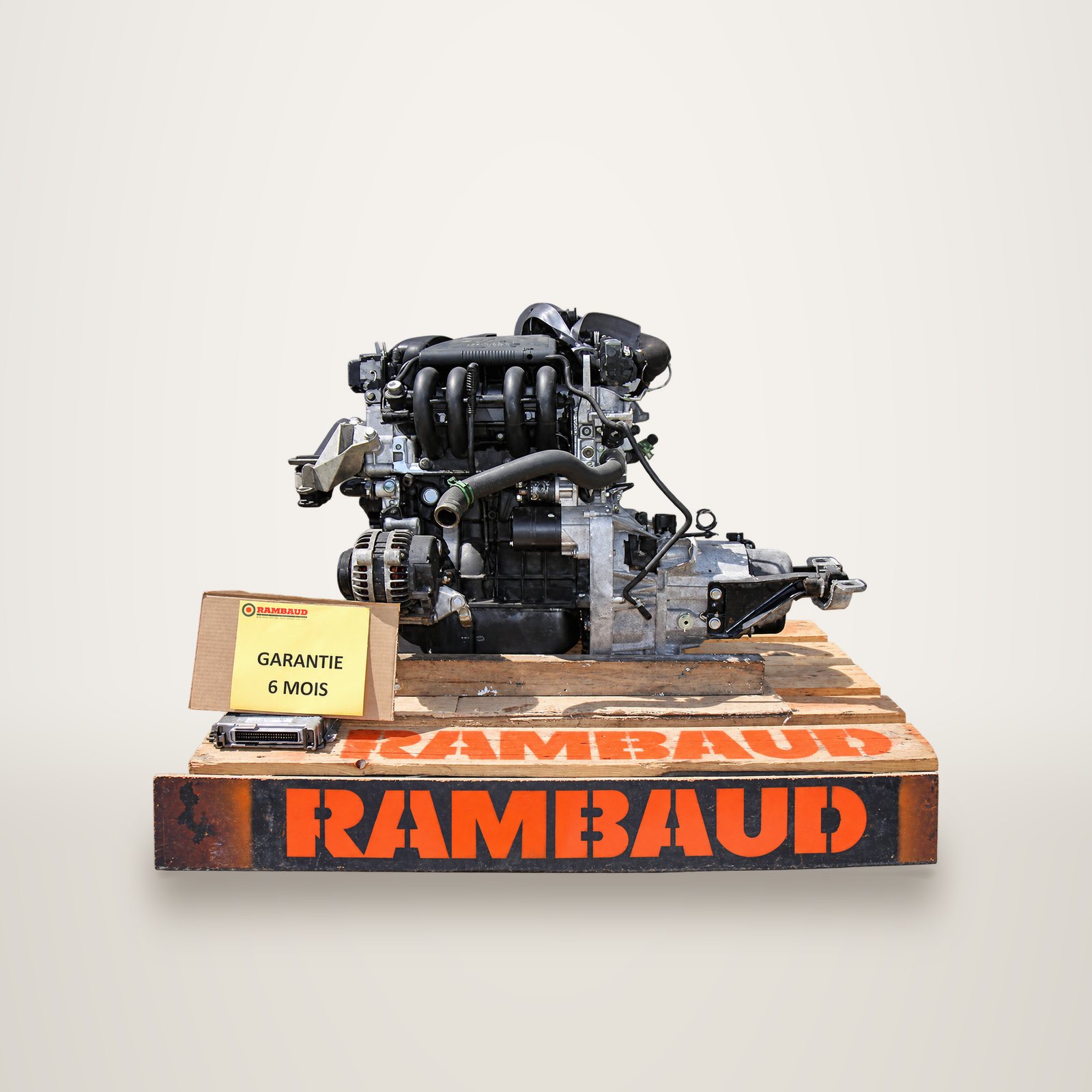 Un moteur d'occasion avec sa boîte de vitesses posé sur une palette en bois estampillée Rambaud, accompagné d'une étiquette indiquant une garantie de 6 mois.