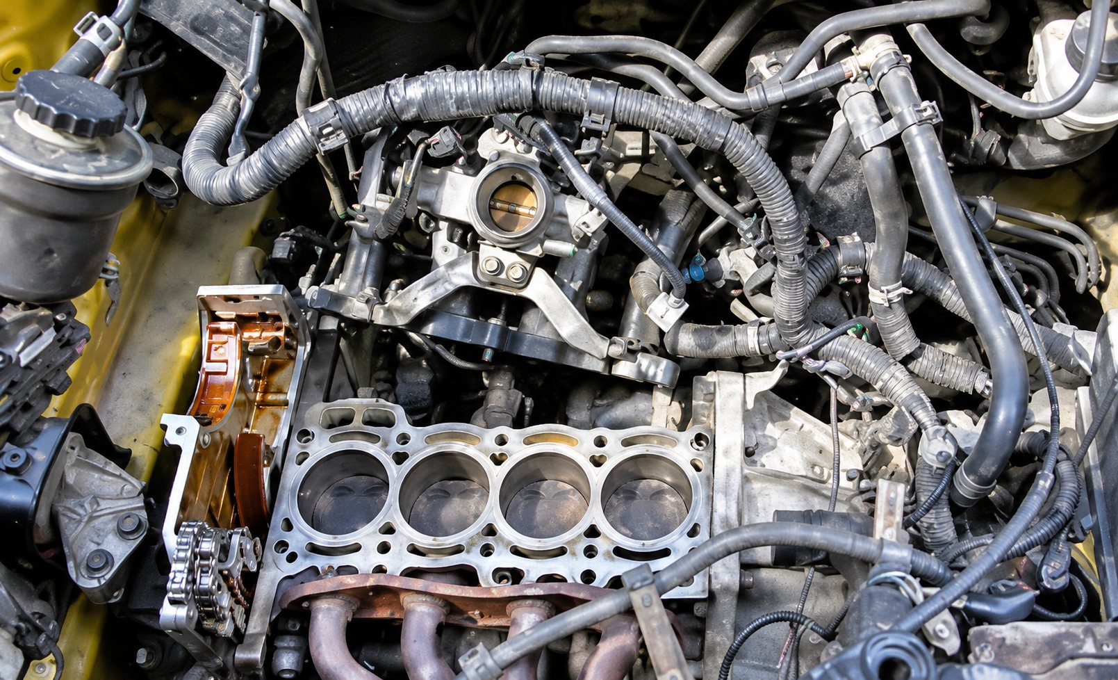 Vue du dessus d'un moteur à quatre cylindres dont la culasse a été déposée, laissant apparaître le haut du bloc et les durites environnantes.