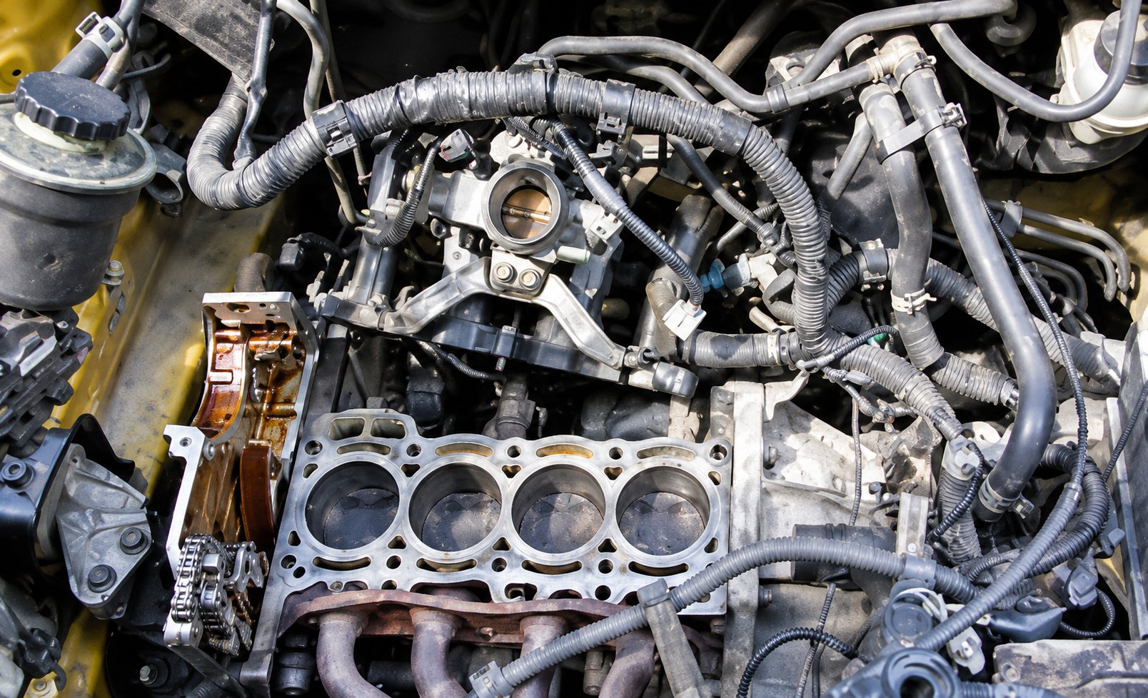 Vue du dessus d'un moteur à quatre cylindres dont la culasse a été retirée, entouré de durites et de composants mécaniques.