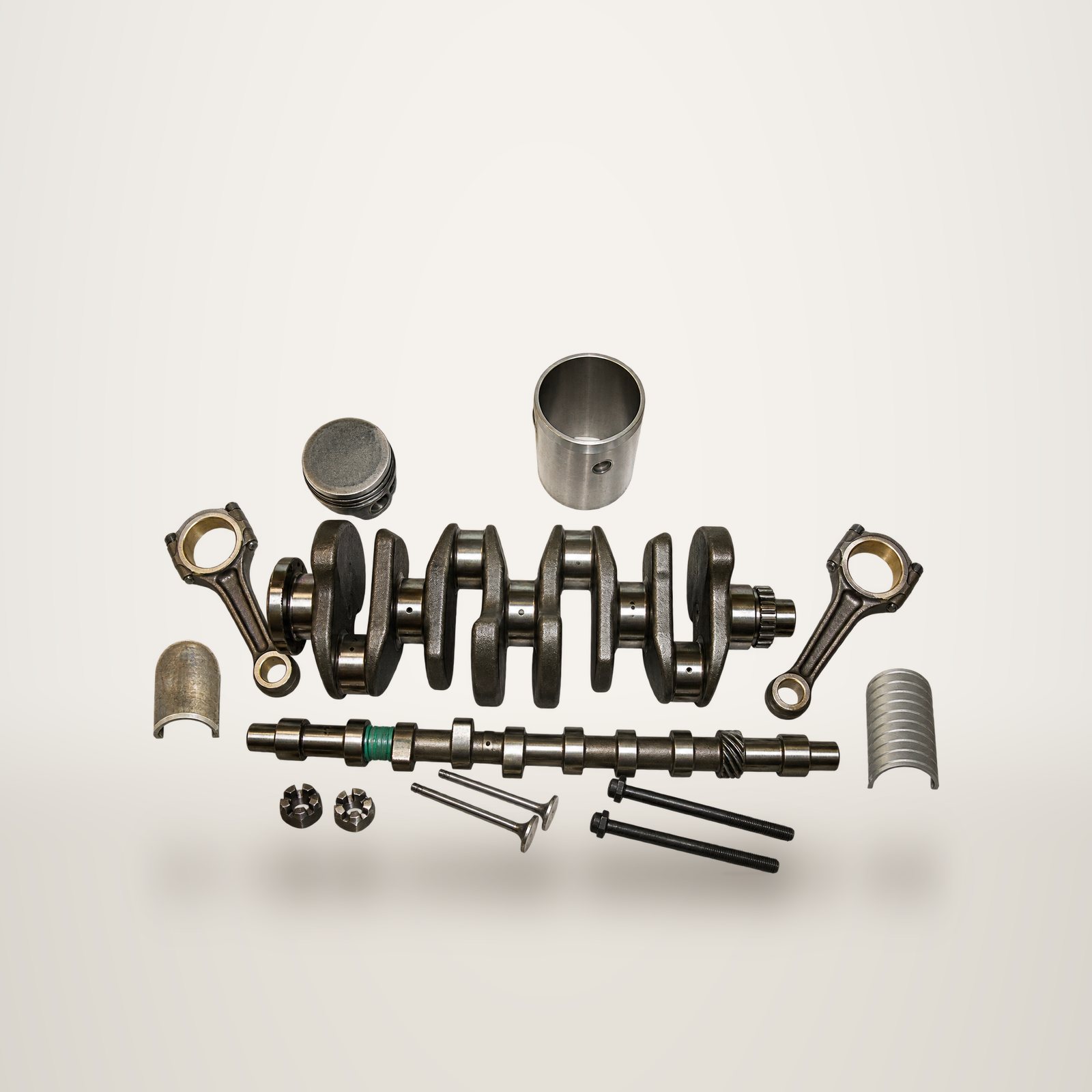Pièces détachées d'un moteur disposées sur un fond blanc, dont un vilebrequin, des bielles, des pistons, un arbre à cames et des soupapes.