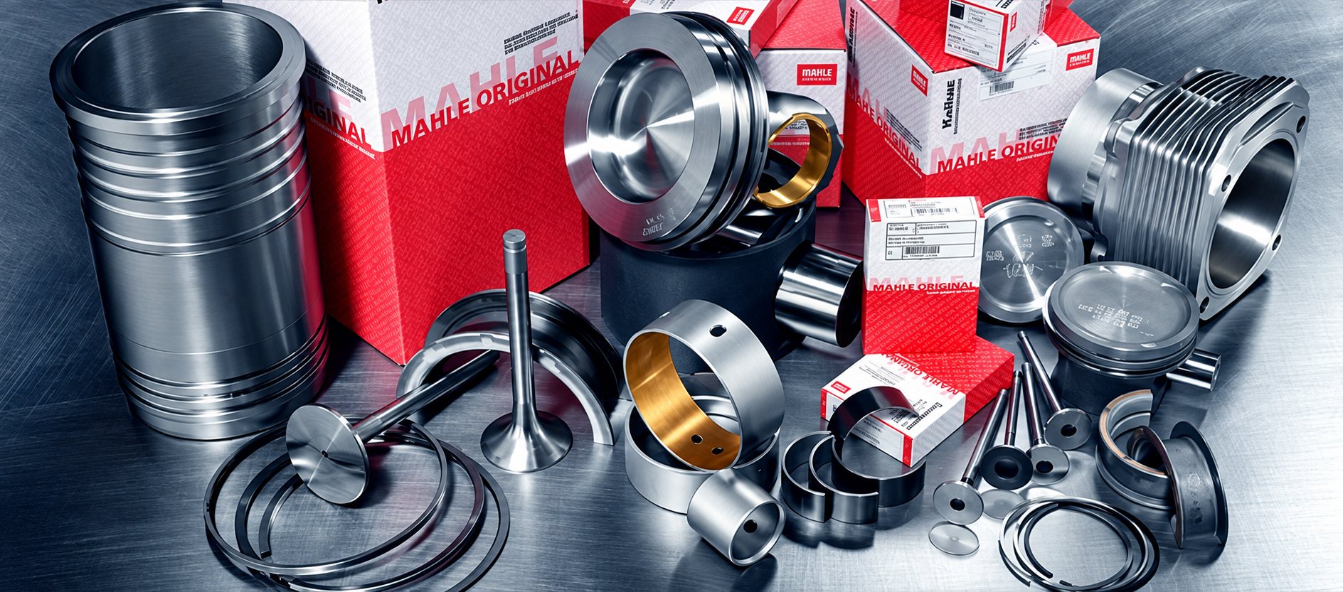 Assortiment de pièces moteur métalliques Mahle, dont pistons, chemise de cylindre, soupapes, bagues et segments, disposé devant des boîtes rouges et blanches.